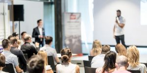 Crowded conference of businesspeople listening to a speaker holding a microphone at a conference