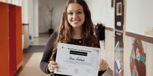 Smiling woman in elementary school hallway holding a Certificate of Completion from the Career Counseling Department.