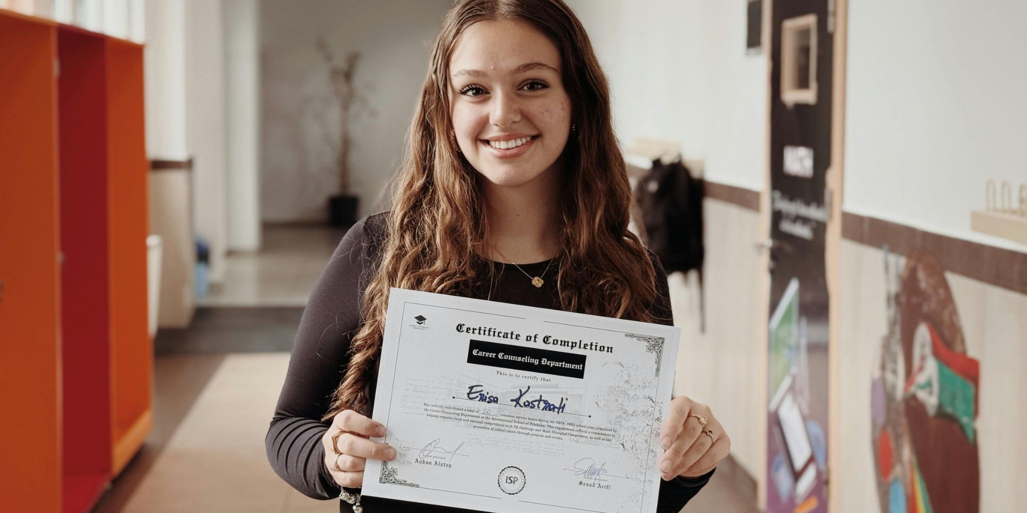 Smiling woman in elementary school hallway holding a Certificate of Completion from the Career Counseling Department.