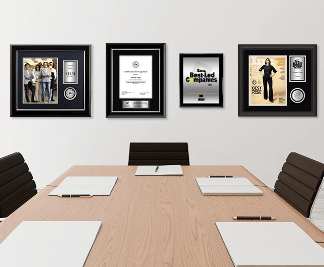 Conference room with a wooden meeting table and a wall displaying framed business awards, certificates, and magazine recognition pieces.