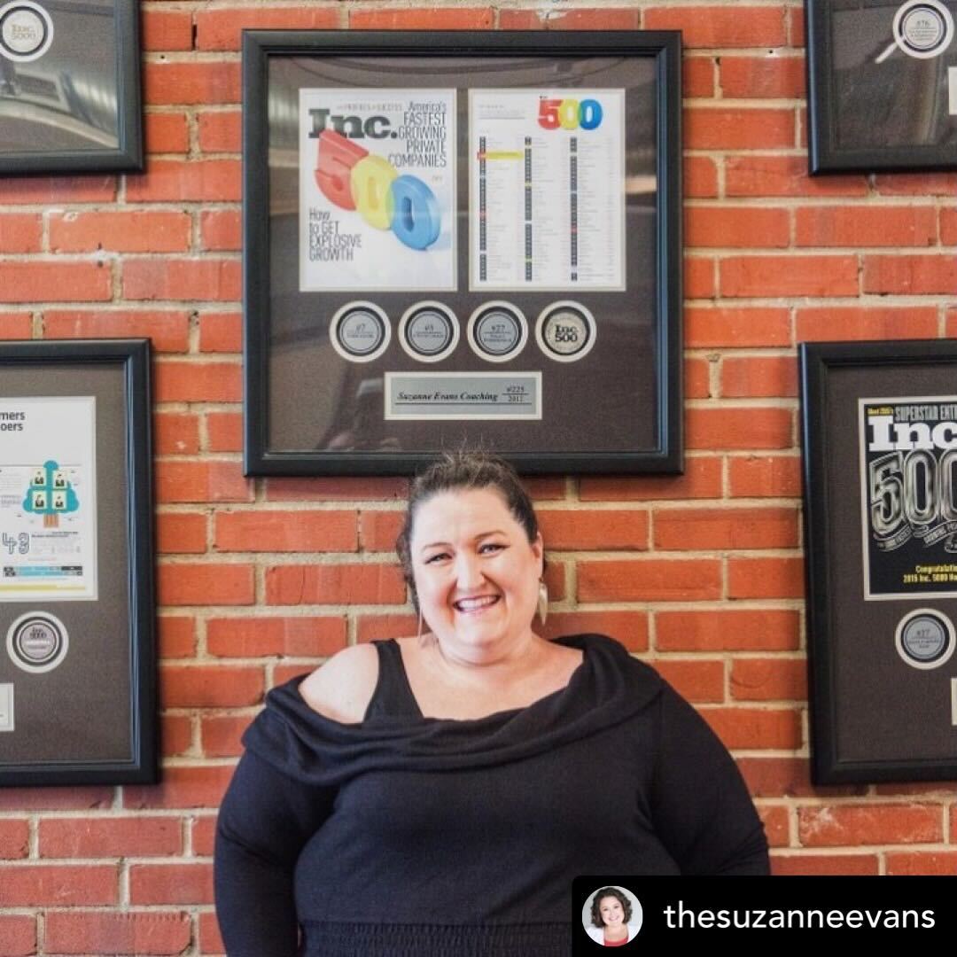 Woman posing in front of a brick wall decorated with framed Inc. 5000 awards and company achievement plaques.