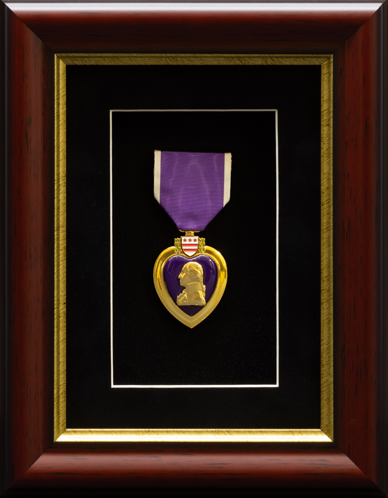 Framed Purple Heart military medal mounted against a black background with gold trim inside a dark wood shadow box.