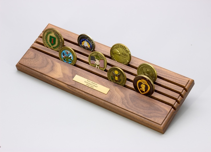 Wooden challenge coin display stand holding multiple military and government commemorative coins with an engraved dedication plaque.