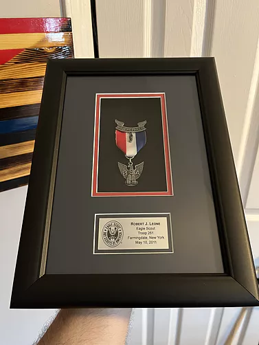 Framed military recognition display featuring a medal, engraved nameplate, and service insignia mounted against a black mat background.