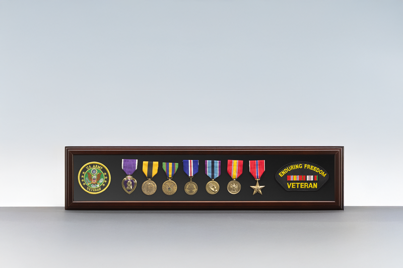 Long wooden shadow box displaying military service medals, ribbons, veteran insignia, and commemorative patches against a black background.