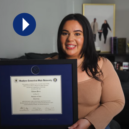 Smiling woman holding her framed diploma, next to a play icon (video thumbnail)