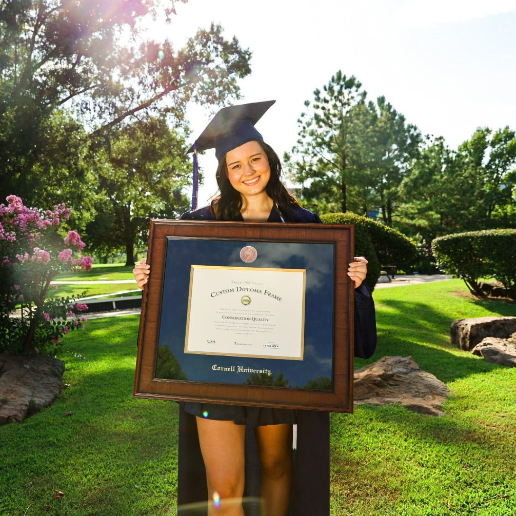 Happy Cornell Grad holding a premium Cornell diploma frame while wearing  her Cornell regalia