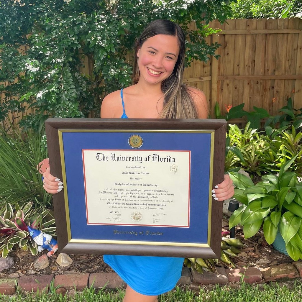 Smiling grad holding UF diploma frame
