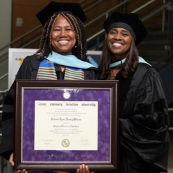Two smiling women in grad regalia with TSCU degree frame