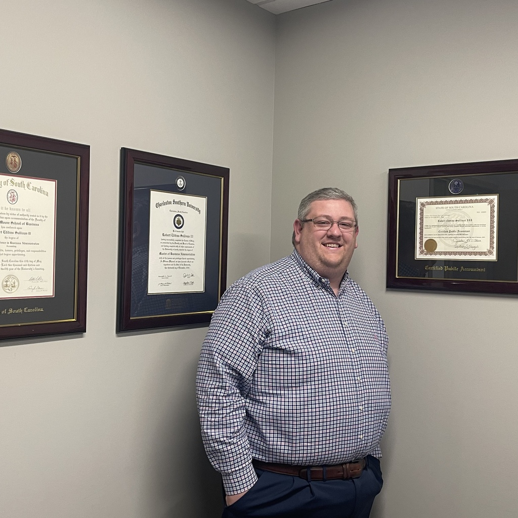 smiling man next to CPA certificate frame on wall