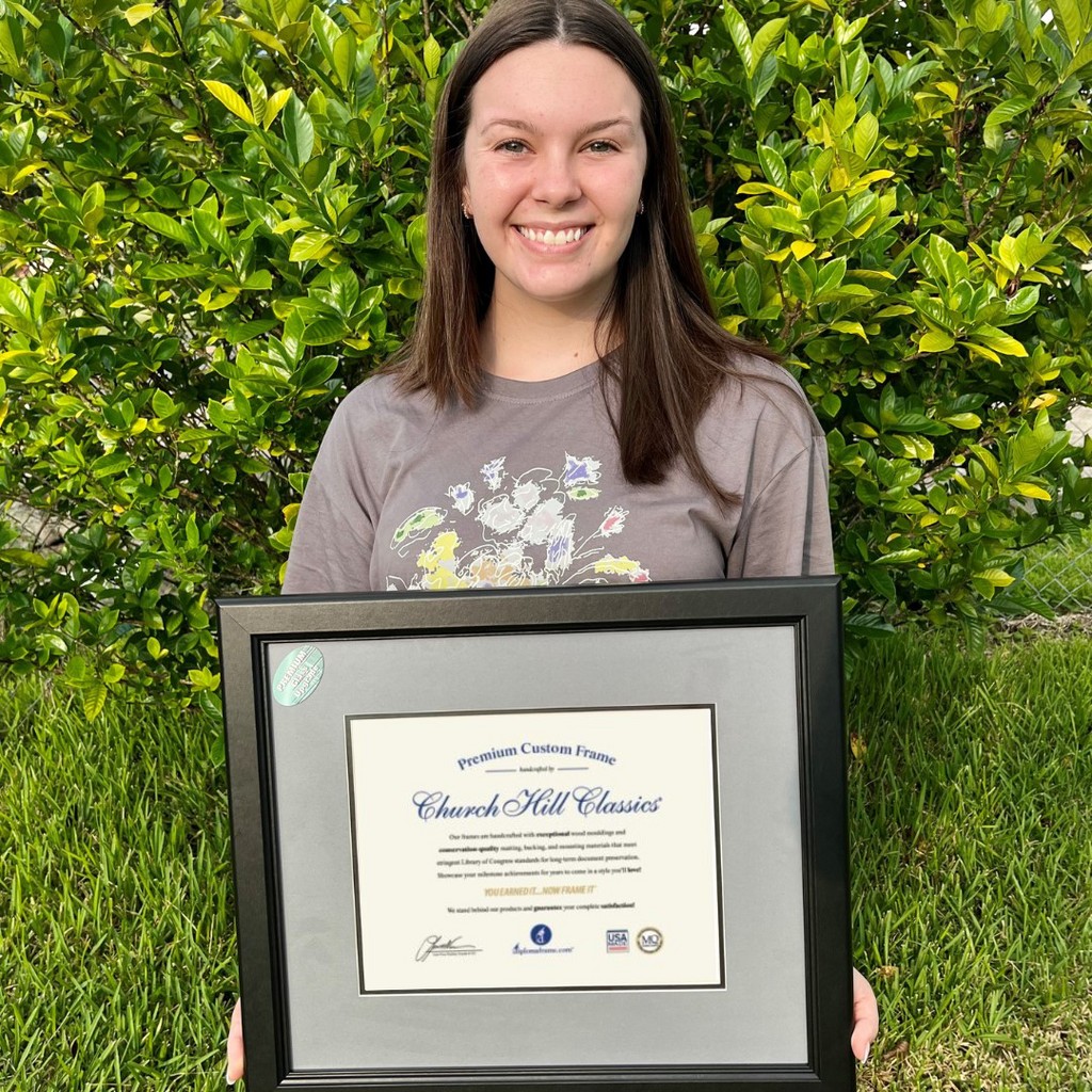 smiling girl holding gray document frame in front of bush