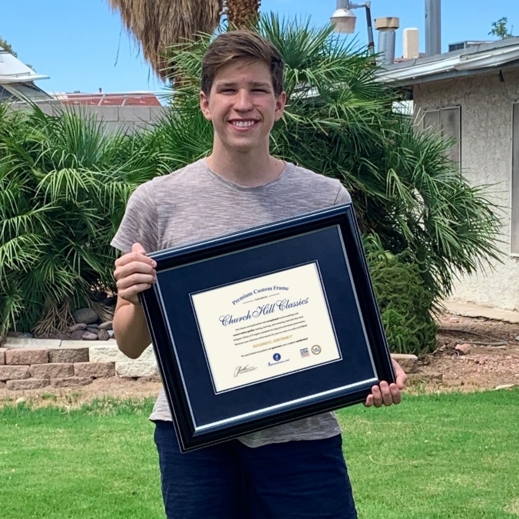 smiling man holding navy blue document frame outdoors