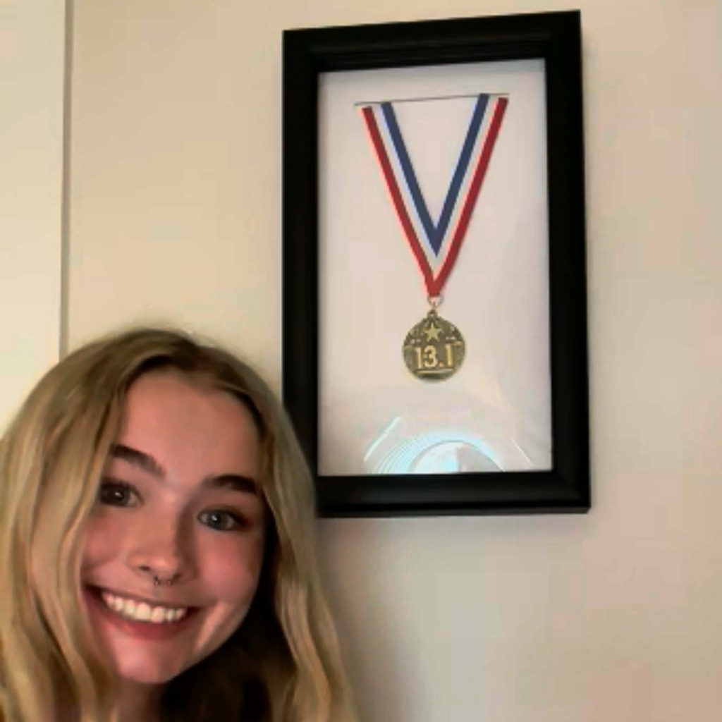 Smiling blonde girl next to marathon medal frame on wall