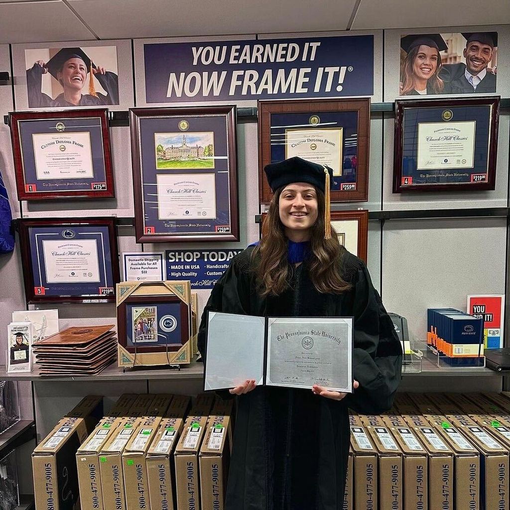 Penn State grad in bookstore in front of wall of PSU diploma frames