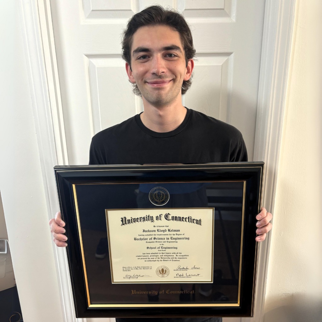 smiling man holding UCONN diploma frame in front of white door