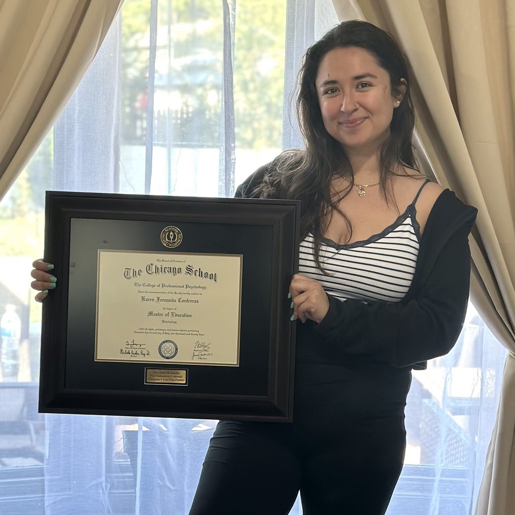 smiling woman holding the chicago school diploma frame in front of window