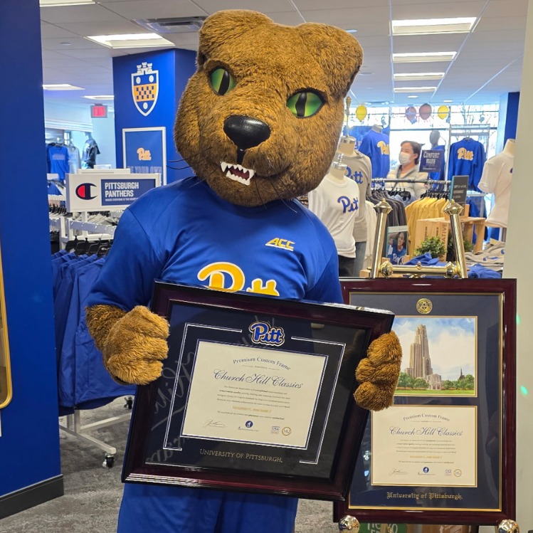 UPitt's Roc the Panther mascot holding a University of Pittsburgh diploma frame in the college bookstore