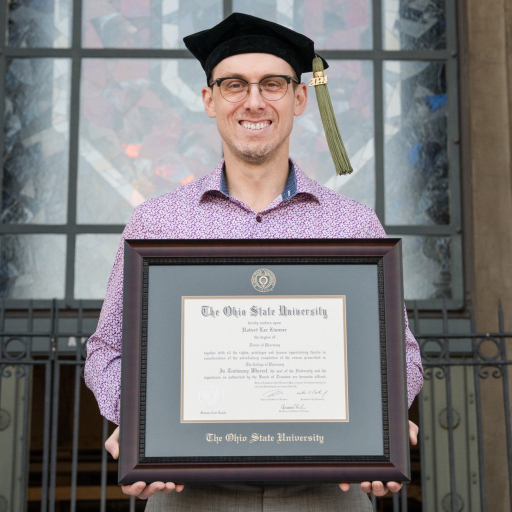 Smiling grad wearing mortarboard and holding Ohio State University diploma frame