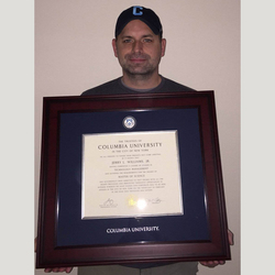 a man wearing a Columbia hat holding a custom Columbia University diploma frame