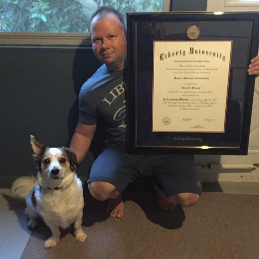 smiling man holding a Church Hill Classics Liberty University diploma frame next to a dog