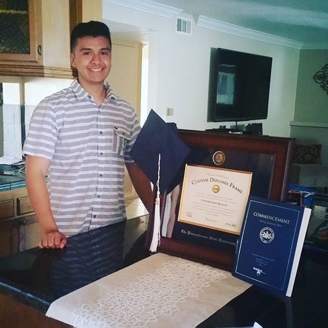 smiling graduate next to a Pennsylvania State University diploma frame with regalia beside it on a table
