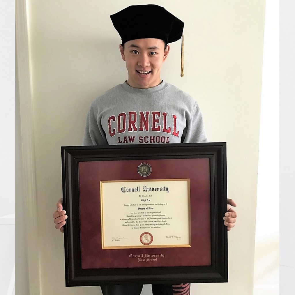 smiling graduate wearing a graduation cap holding a custom Cornell University diploma frame