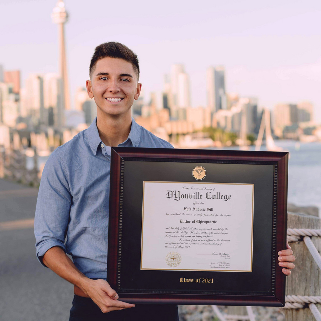 smiling man holding a custom diploma frame with a city skyline in the background